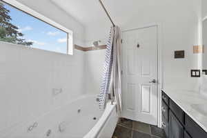 Bathroom with a combined bath / shower with jetted tub, vanity, and dark stone finish flooring