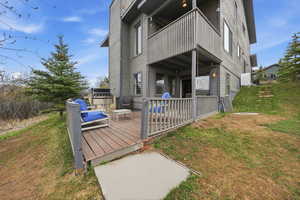 Back of house featuring a wooden deck, a lawn, a balcony, and a patio