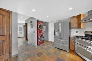 Kitchen featuring stainless steel appliances, wood finish cabinetry, stacked washing machine and dryer, light stone counters, and tasteful backsplash