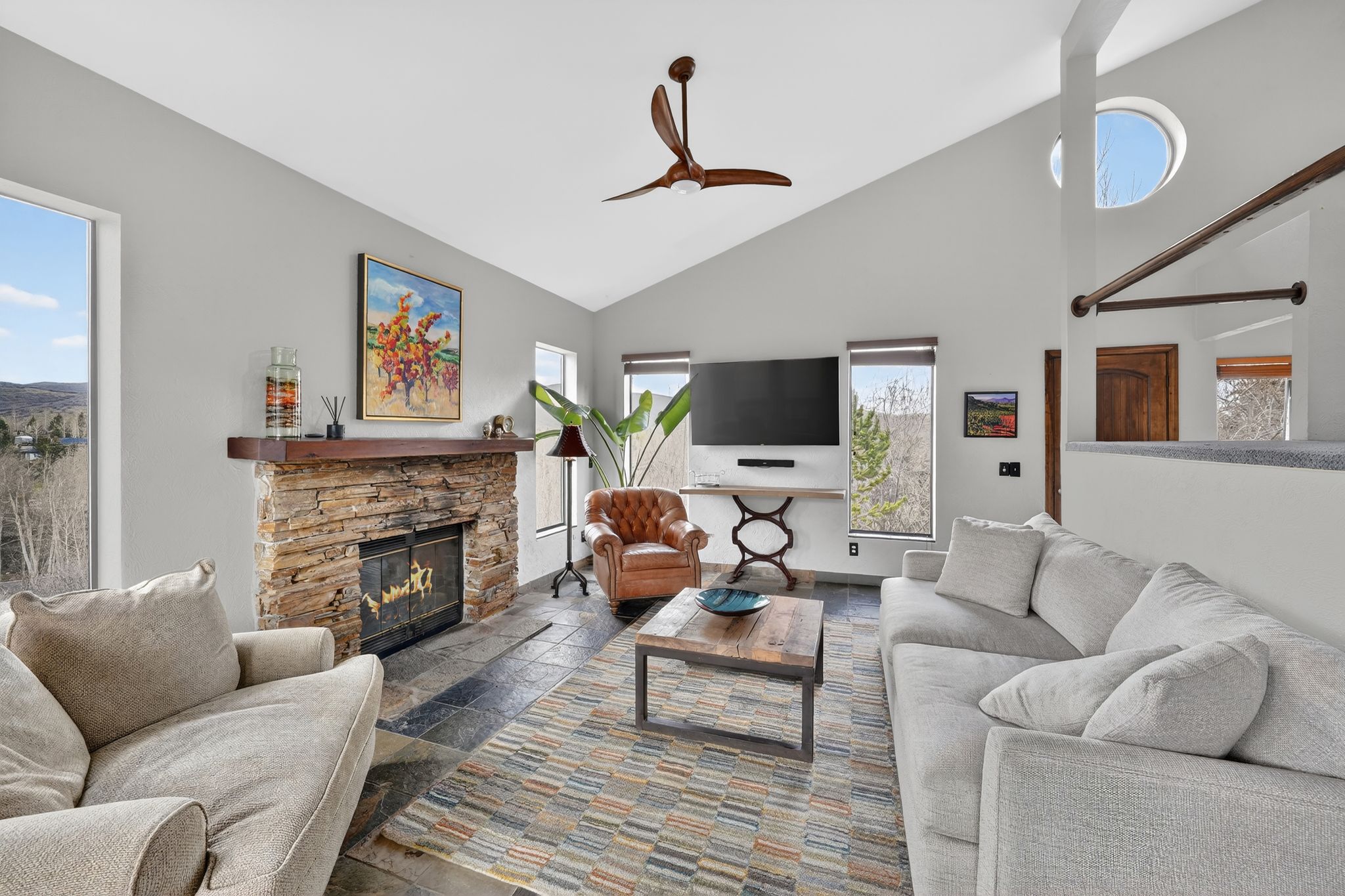 Living area featuring stone tile floors, a fireplace, lofted ceiling, and a ceiling fan