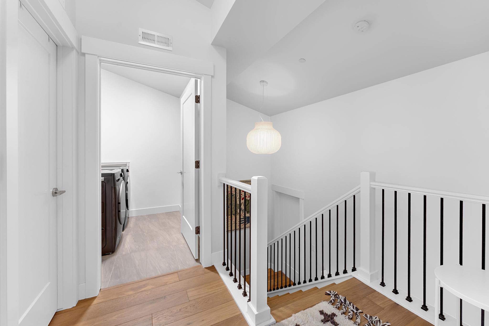 Hallway with light wood-style floors, separate washer and dryer, an upstairs landing, and vaulted ceiling