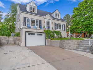 New england style home with driveway, a garage, brick siding, a balcony, and roof with shingles