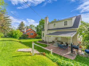 Rear view of property featuring a patio, roof with shingles, a yard, and a chimney