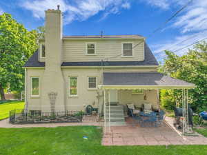 Rear view of house with a patio area, brick siding, roof with shingles, and a chimney