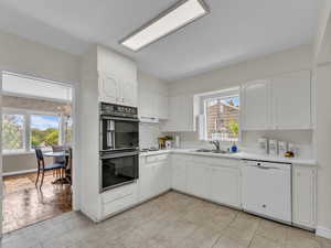 Kitchen with white dishwasher, light countertops, white cabinetry, hanging lights, and ventilation hood