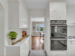 Kitchen featuring white cabinetry, arched walkways, light countertops, and range hood