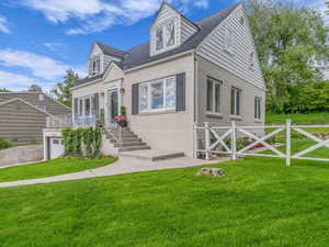 New england style home featuring a front yard, brick siding, and roof with shingles