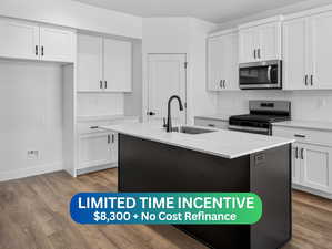 Dual tone kitchen featuring stainless steel appliances, an island with sink, light stone counters, tasteful backsplash, and wood finished floors