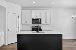 Kitchen with light stone counters, dark wood-style floors, stainless steel appliances, a center island with sink, and two tone cabinetry