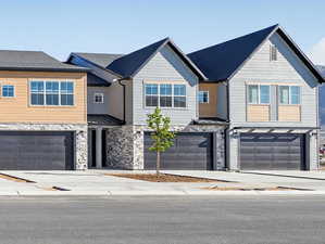 View of front of house with stone siding, a garage, concrete driveway, and a shingled roof