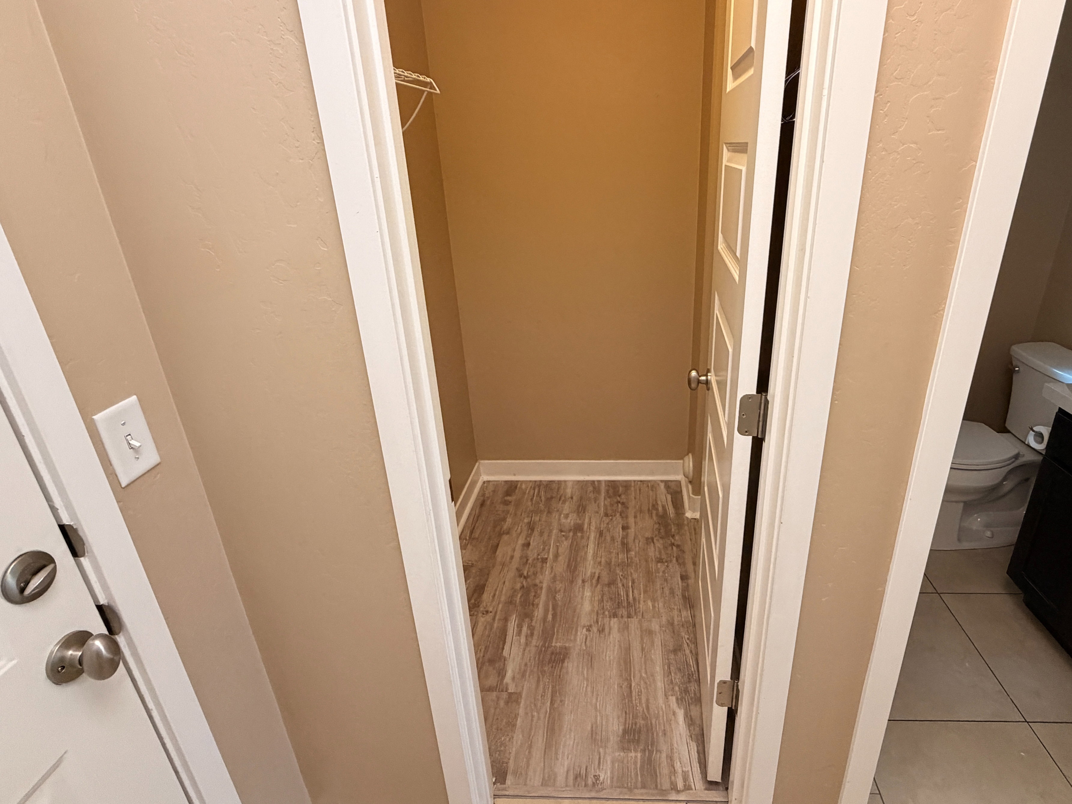 Compact storage closet with wood-finish flooring, featuring a single wire shelf. Optional upgrade in unit.