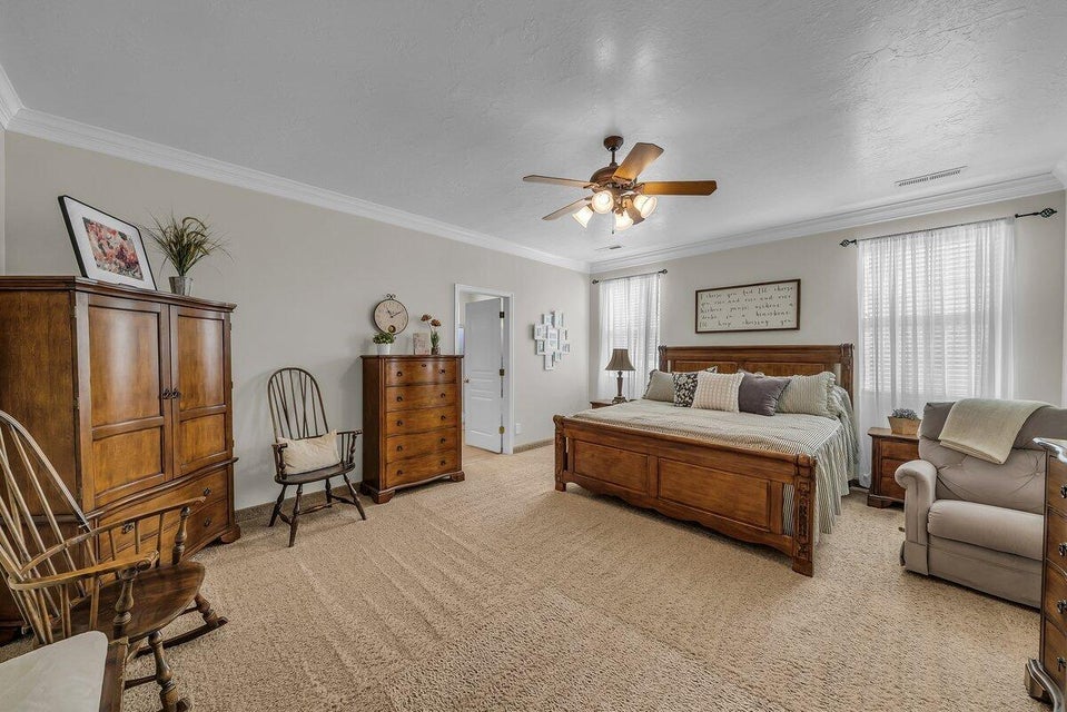 Bedroom with ceiling fan, light colored carpet, and ornamental molding