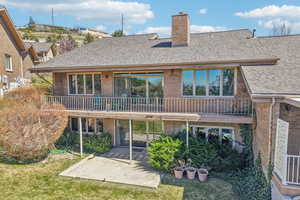 Rear view of house with a balcony, brick siding, a chimney, a shingled roof, and a yard