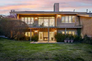 Back of house with a chimney, brick siding, a balcony, a lawn, and a patio area