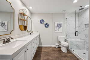 Bathroom with double vanity, dark wood-type flooring, a marble finish shower, and recessed lighting