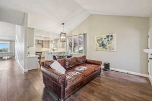 Living room featuring dark wood finished floors, a chandelier, and lofted ceiling