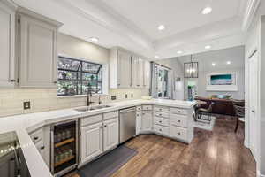 Kitchen with beverage cooler, dark wood finished floors, stainless steel dishwasher, tasteful backsplash, and a raised ceiling