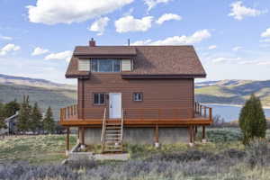 Back of property with a deck with mountain view, a shingled roof, and a chimney