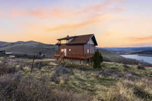 Back of house at dusk featuring a deck with water view and a chimney
