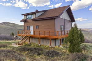 Back of house featuring a deck with mountain view, a chimney, and roof with shingles