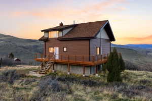 Back of house at dusk with a deck with mountain view, a chimney, and a shingled roof