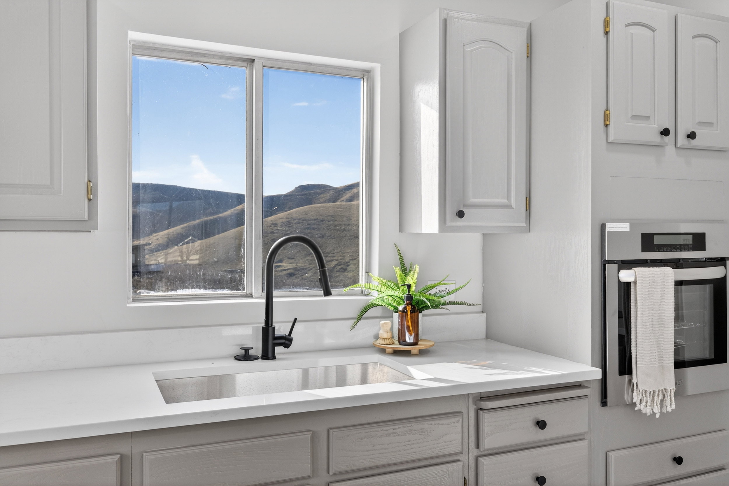Kitchen with oven, white cabinets, light stone countertops, and a mountain view