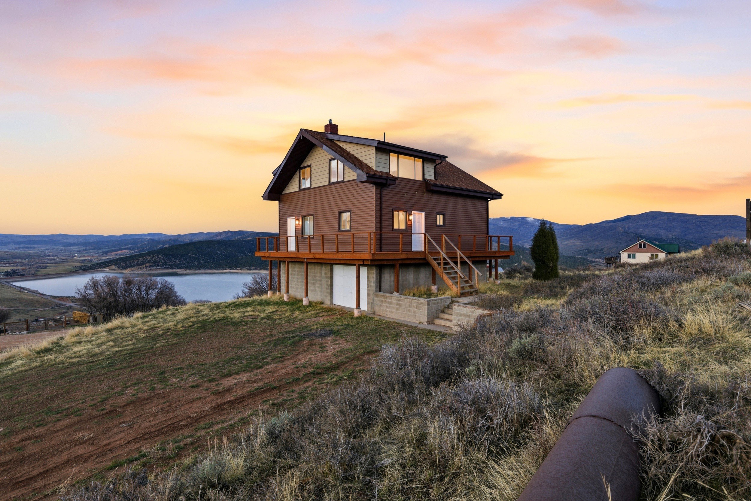 Back of house at dusk featuring a chimney, a deck with water view, and a garage
