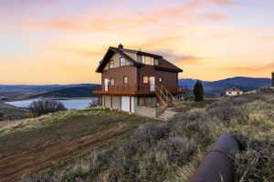 Back of house at dusk featuring a chimney, a deck with water view, and a garage