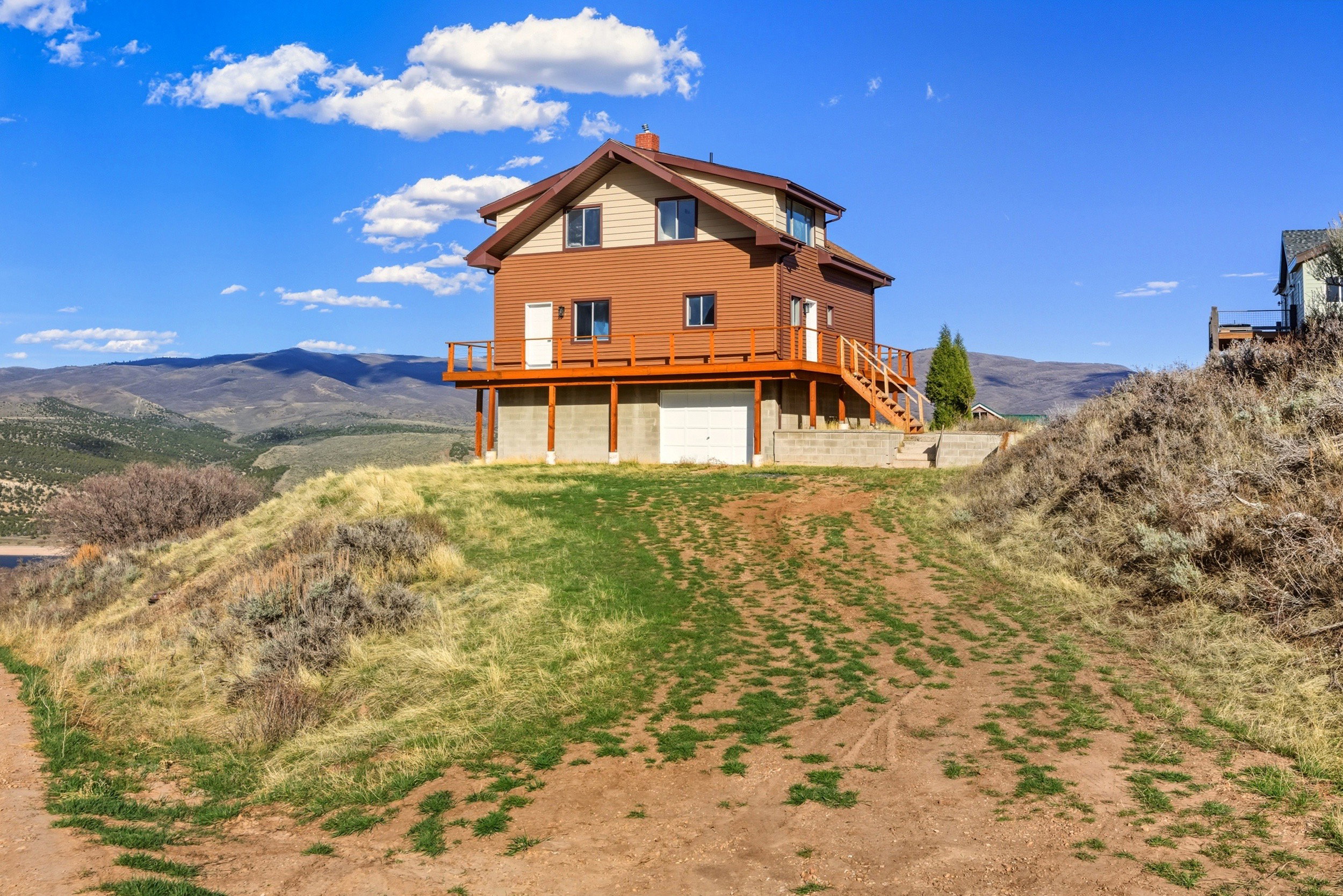 Rear view of property featuring a chimney, a garage, a deck with mountain view, and driveway