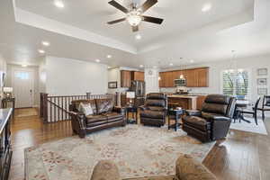 Living area with a tray ceiling, dark wood-style floors, and ceiling fan
