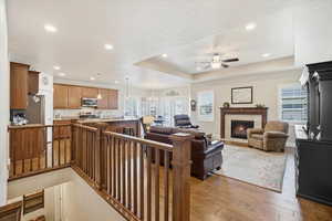 Great room with light wood floors, gas fireplace, a ceiling fan, plenty of natural light, and a raised ceiling