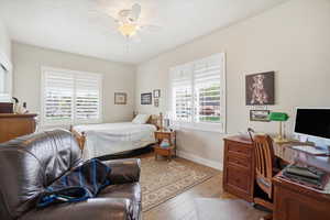 Bedroom featuring hardwood / wood-style flooring, multiple windows, an office area, and a ceiling fan