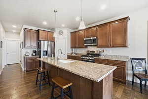 Kitchen featuring stainless steel appliances, pendant lighting, a breakfast bar area, an island with sink, and light stone countertops