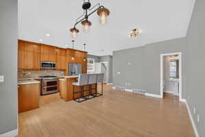 Kitchen featuring stainless steel appliances, a center island, light wood-style floors, decorative light fixtures, and a breakfast bar