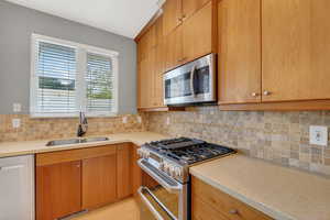 Kitchen with stainless steel appliances, light stone counters, backsplash, and wood finish cabinets