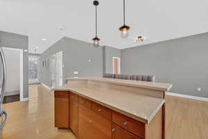 Kitchen with wood finish cabinets, light wood-type flooring, light stone counters, a kitchen island, and pendant lighting