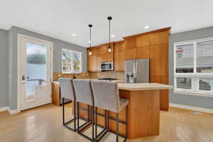 Kitchen featuring a breakfast bar, light countertops, light wood-style flooring, stainless steel appliances, and hanging light fixtures