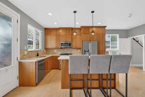 Kitchen with a breakfast bar, stainless steel appliances, a center island, light wood finished floors, and wood finish cabinetry