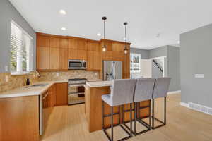 Kitchen with stainless steel appliances, light countertops, light wood-type flooring, and a kitchen bar