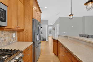 Kitchen featuring stainless steel appliances, light wood-style floors, pendant lighting, wood finish cabinetry, and tasteful backsplash