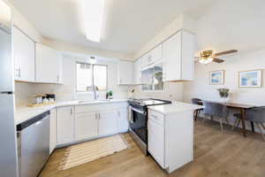 Kitchen featuring stainless steel appliances, white cabinets, light wood-type flooring, and light stone counters
