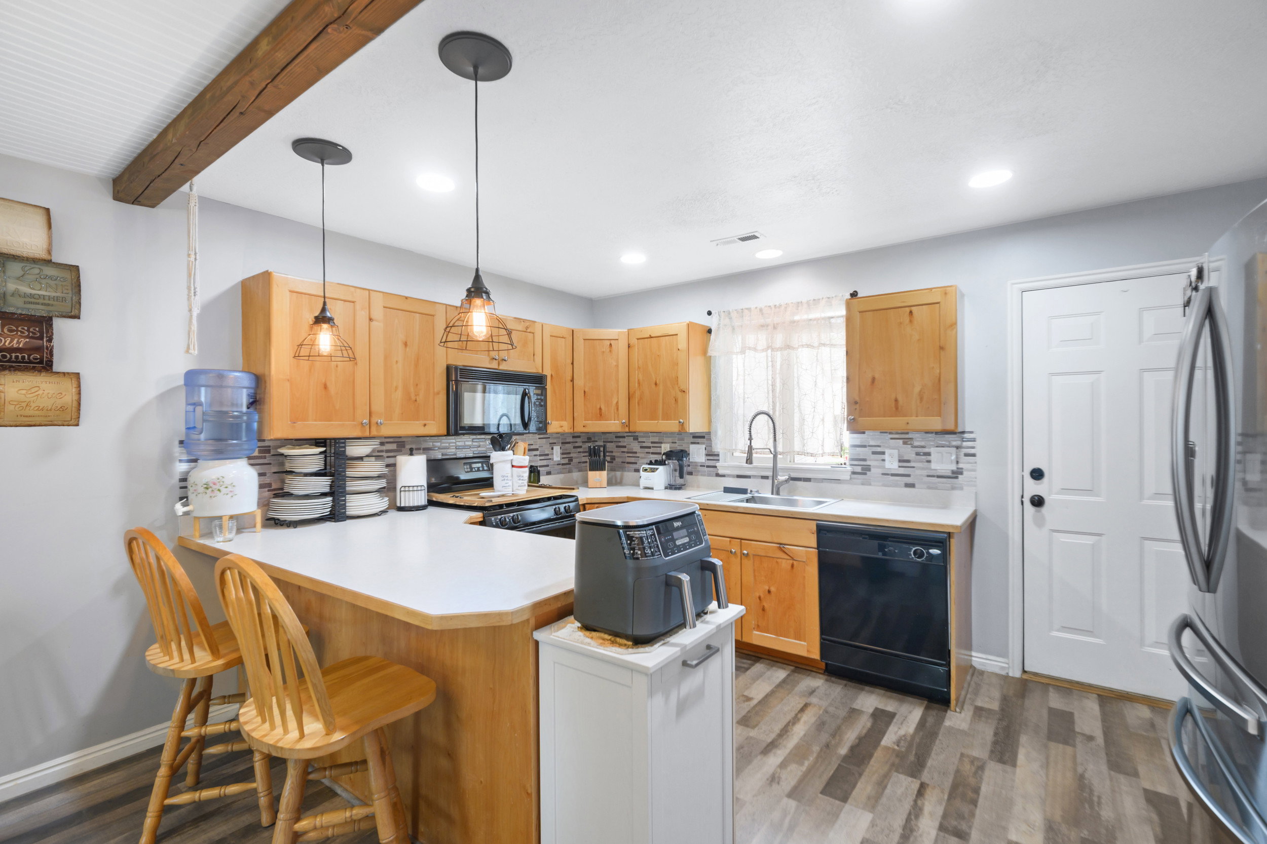 Kitchen with decorative backsplash, light countertops, a peninsula, decorative light fixtures, and a kitchen bar