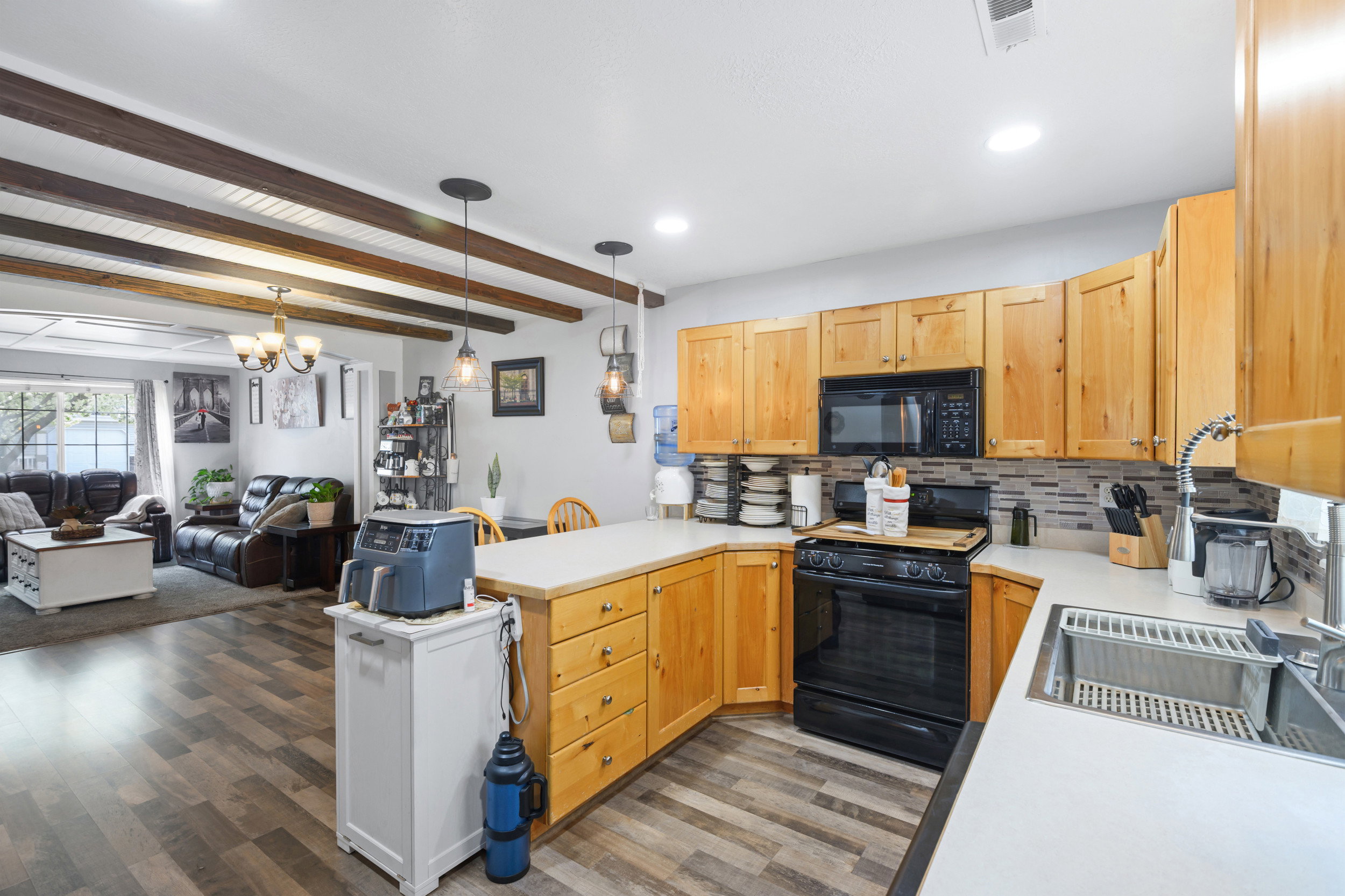 Kitchen featuring light countertops, backsplash, open floor plan, black appliances, and a peninsula