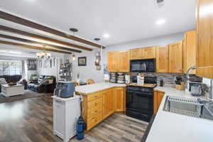 Kitchen featuring light countertops, backsplash, open floor plan, black appliances, and a peninsula
