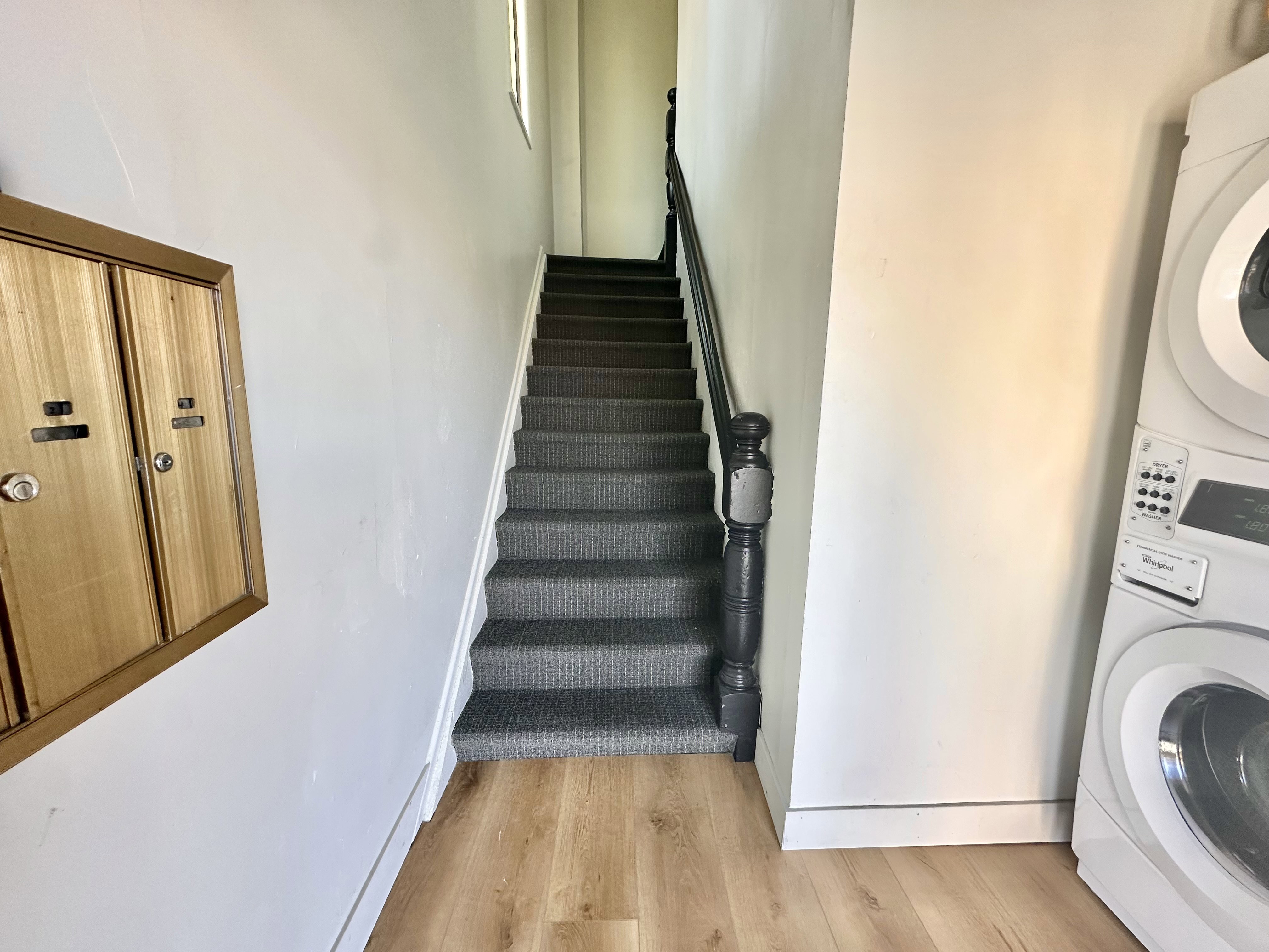 Stairs with wood finished floors and stacked washing machine and dryer