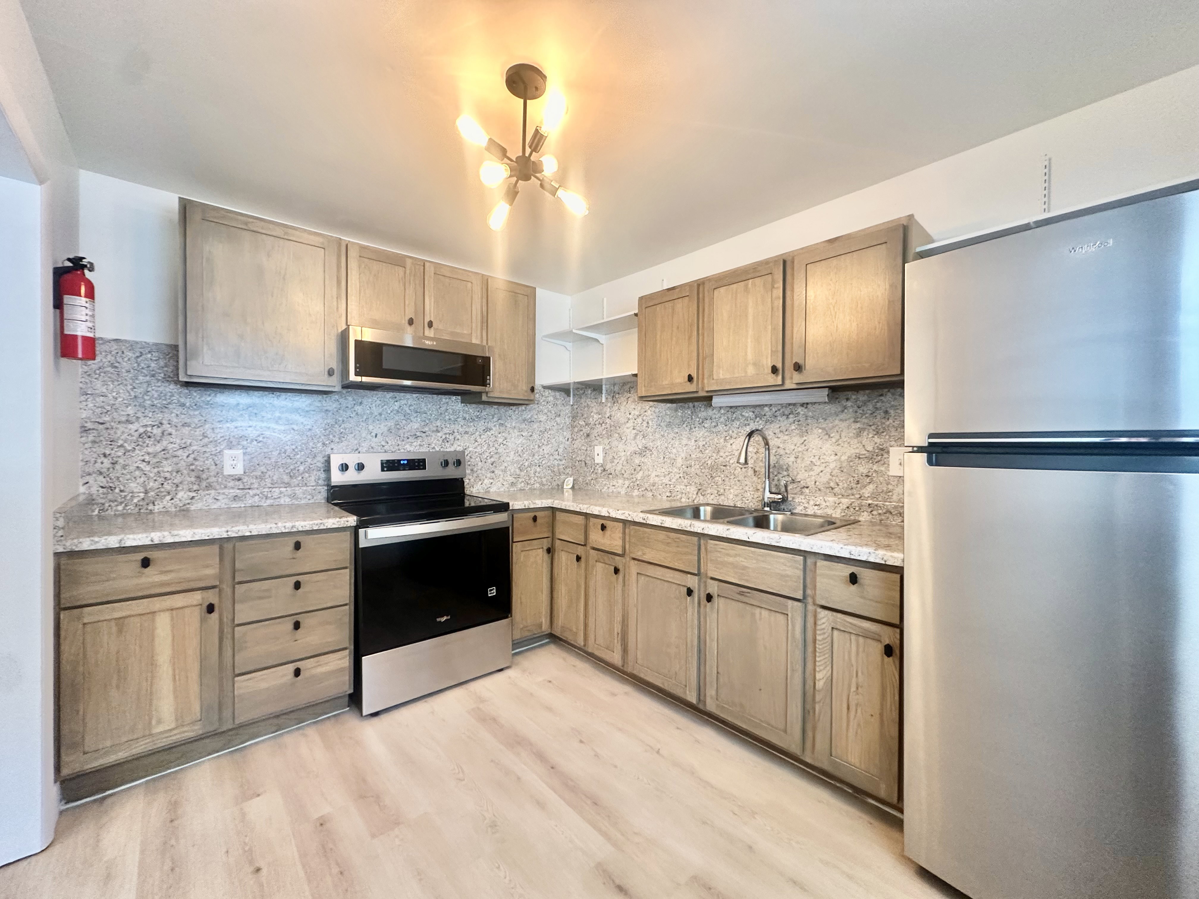 Kitchen featuring light wood-finish cabinetry, light-toned countertops with matching backsplash, stainless steel appliances, and a double basin sink