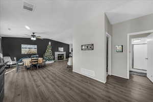 Dining room featuring dark wood-style flooring, lofted ceiling, ceiling fan, and a warm lit fireplace