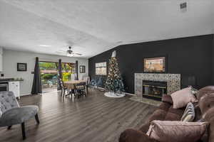Living area featuring dark wood finished floors, a ceiling fan, a tiled fireplace, and vaulted ceiling