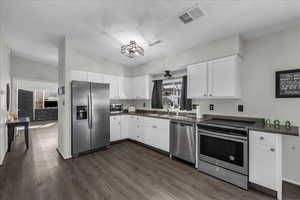 Kitchen with stainless steel appliances, white cabinets, dark wood-type flooring, and lofted ceiling