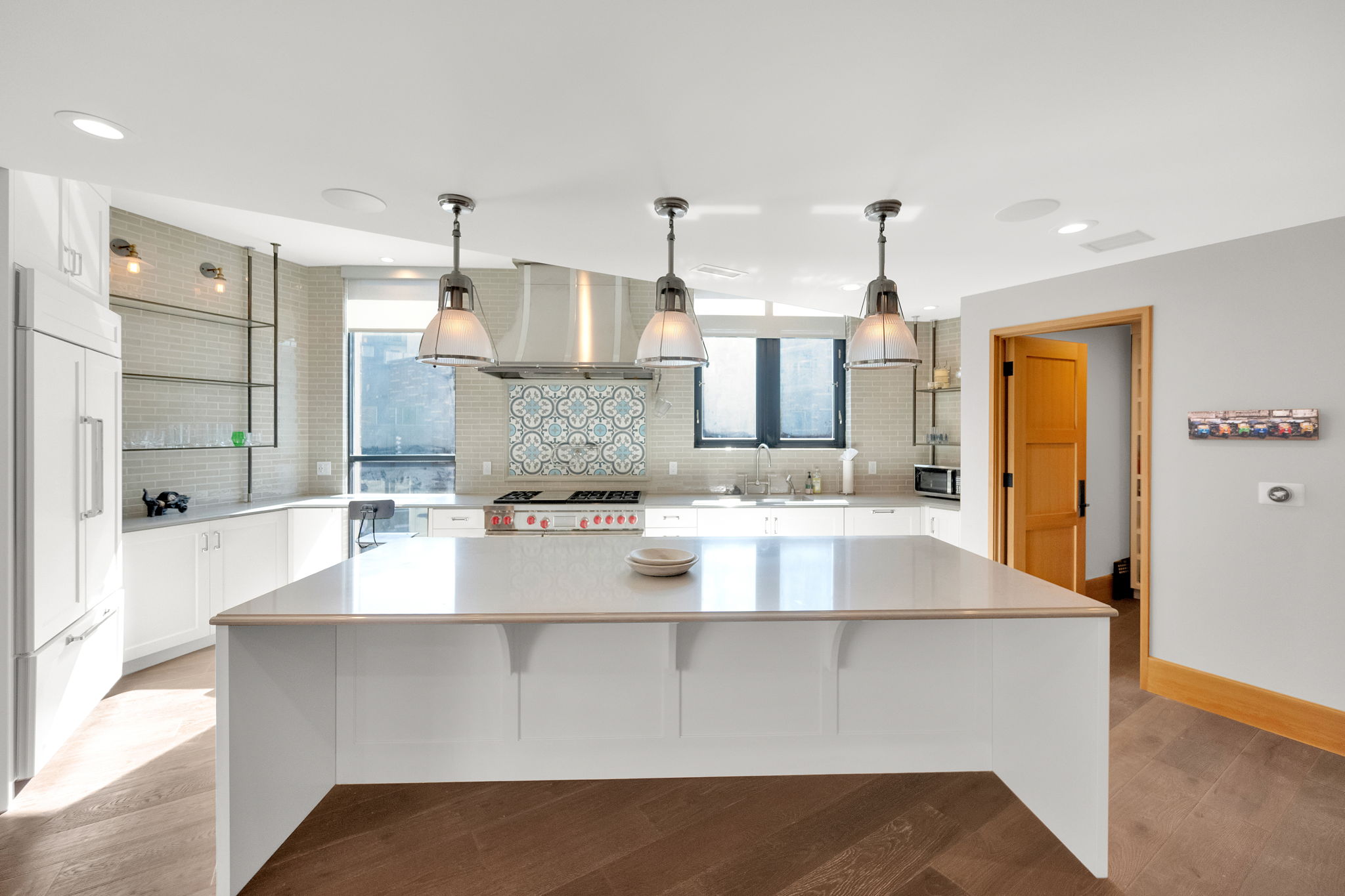 Kitchen featuring a large island, backsplash, white cabinets, stainless steel appliances, and light stone countertops